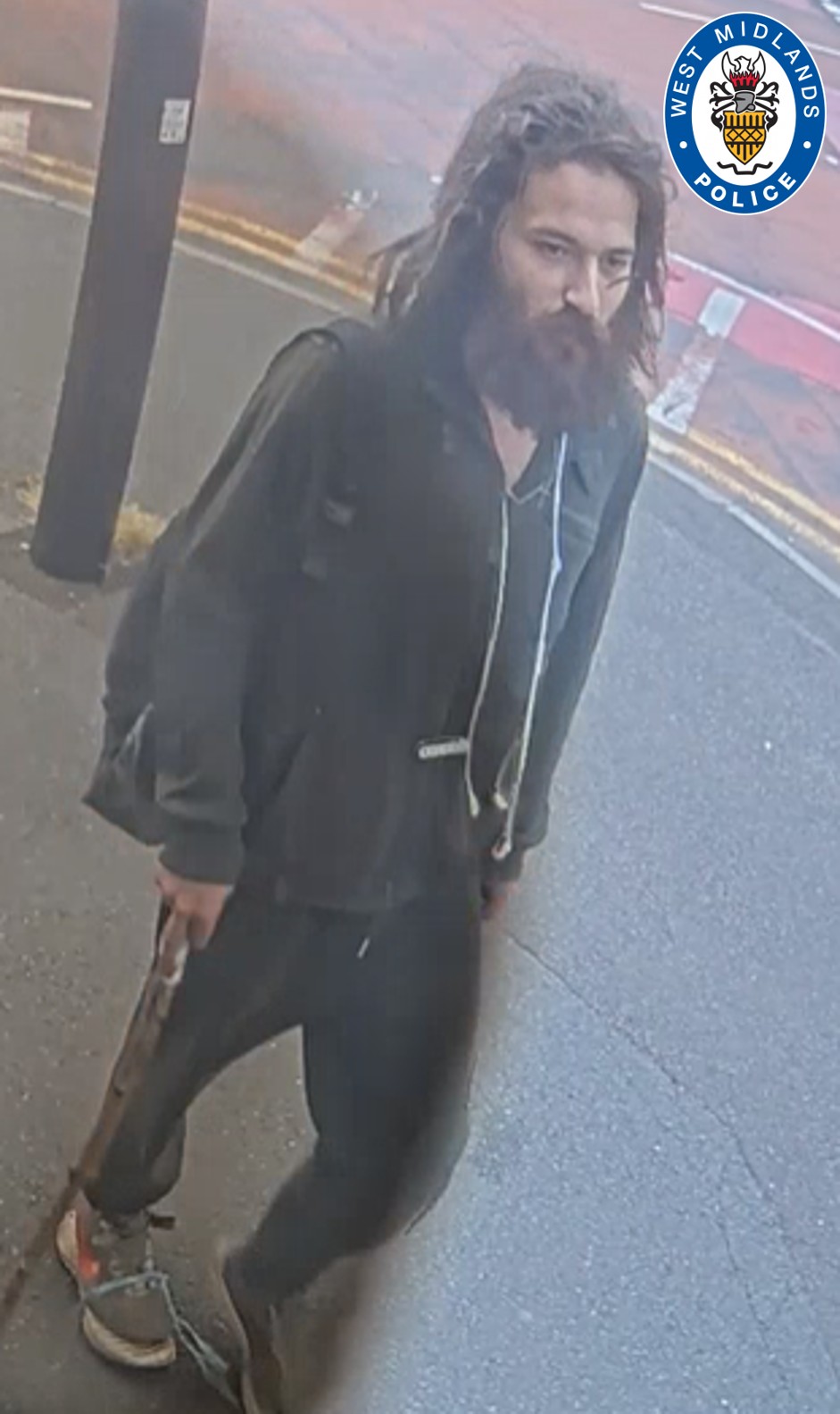 CCTV image of a man stood on street wearing a dark hoodie, black joggers and grey trainers